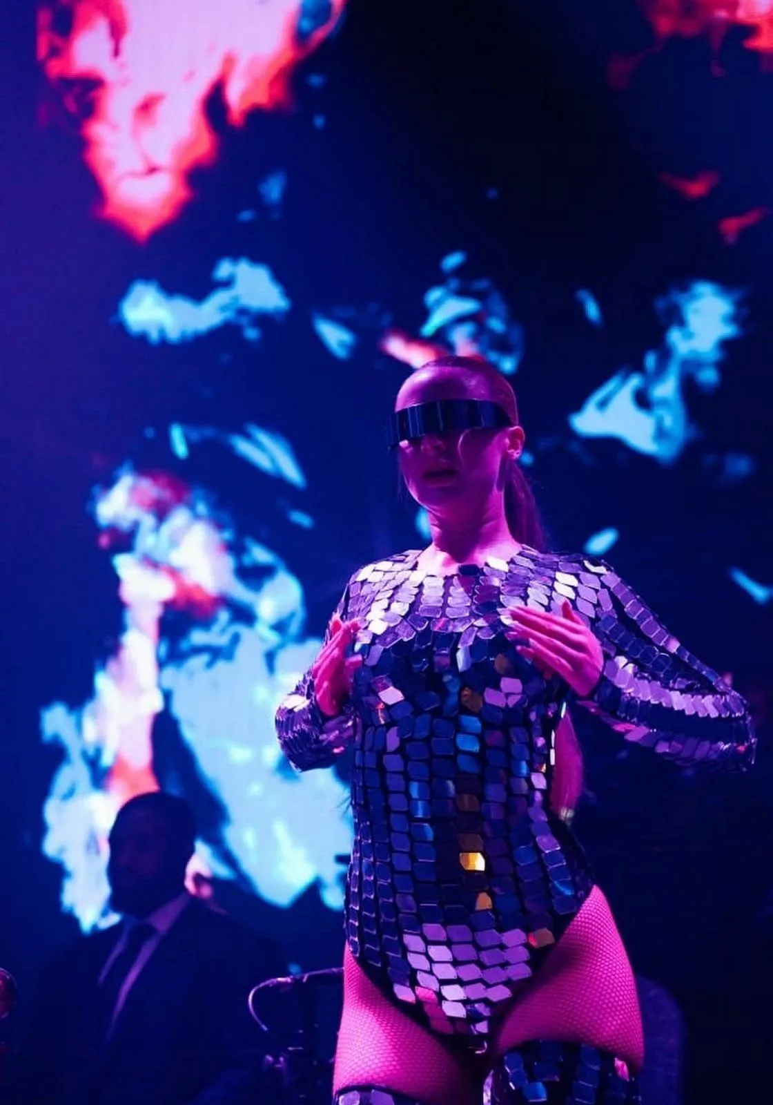 Dancer in a reflective mirrored suit reflecting beam lights across the room