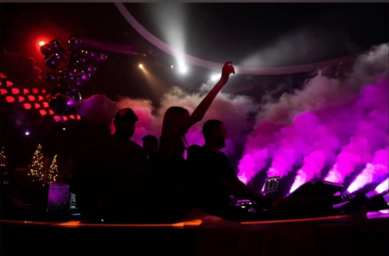 DJ mixing tracks behind the elevated sound booth flanked by stage lighting effects