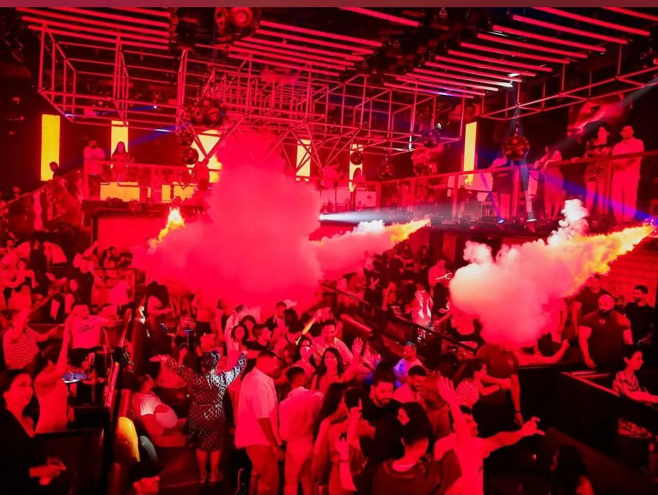 White CO2 plumes bursting over a crowded dance floor with raised hands